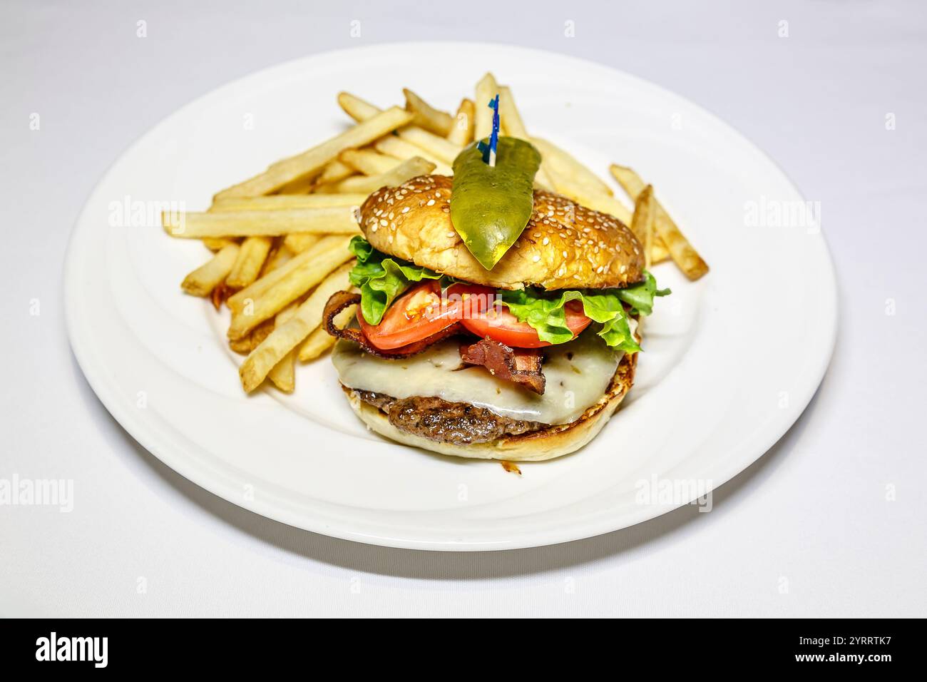 Un hamburger con lattuga e pomodoro su un piatto bianco. Un lato di patatine fritte. L'hamburger è condito con una lancia di sottaceti Foto Stock