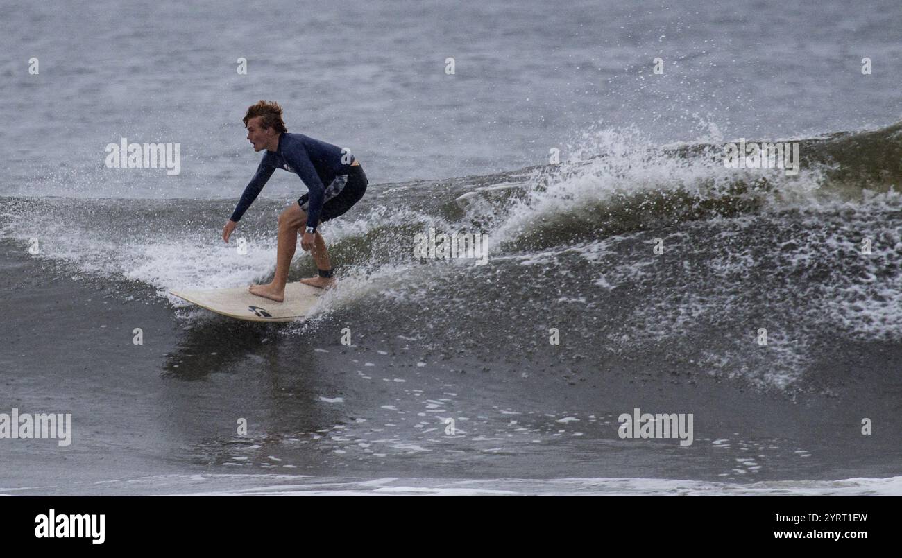 Gilgo Beach, New York, USA - 30 agosto 2023: Un giovane surfista manovra sapientemente su un'onda in spiaggia sotto cieli nuvolosi. Foto Stock