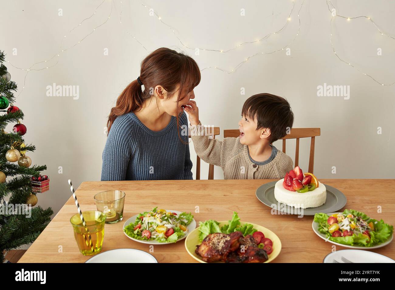 Ragazzo che dà da mangiare alle fragole da una torta a sua madre a una festa di Natale Foto Stock
