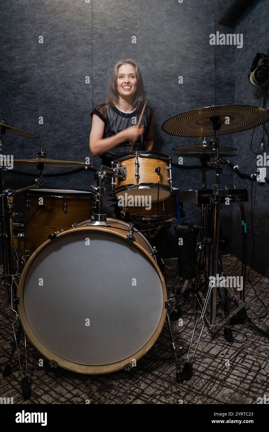 Donna che suona la batteria in studio insonorizzato. Esibizione musicale in sala di studio professionale. Produzione musicale e intrattenimento. Foto Stock