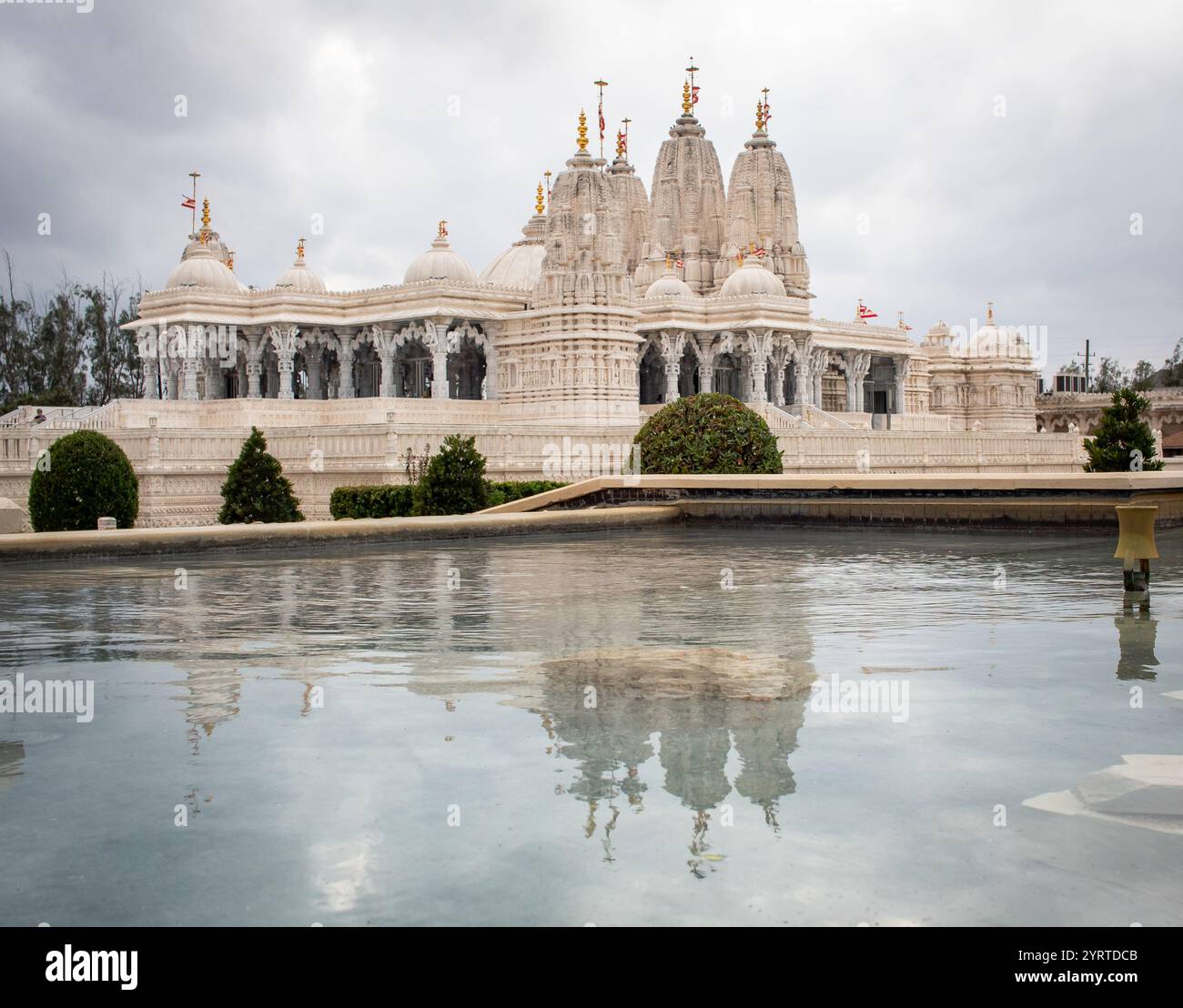 Elaborato tempio bianco BAPS Shri Swaminarayan Mandir circondato da alberi e acqua. Foto scattata a Houston in Texas in una giornata nuvolosa Foto Stock