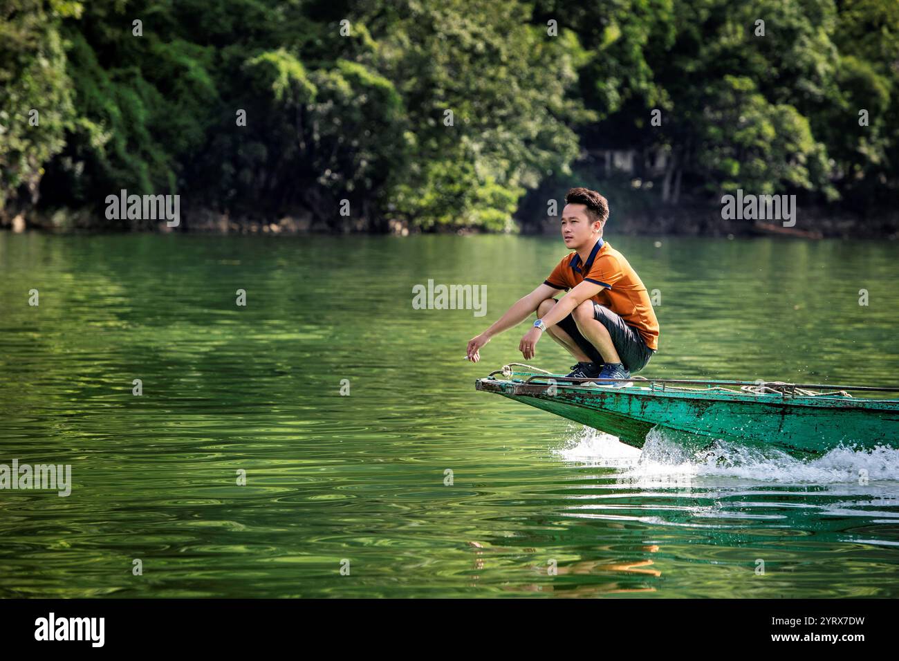 Un uomo seduto sulla prua di una barca che viaggia sul lago Ba Be nel Parco Nazionale di Ba Be nella provincia di Bac Kan, Vietnam Foto Stock