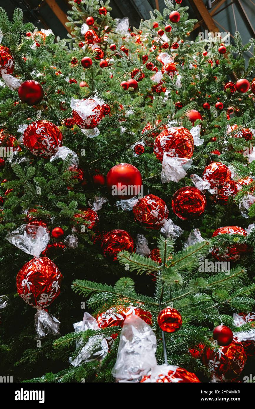 3-12-2024 Zurigo, Svizzera. Grande albero di Natale all'interno della stazione principale di Zurigo decorato con palline di cioccolato Lindt rosse. Primo piano, guarda in alto, no Foto Stock