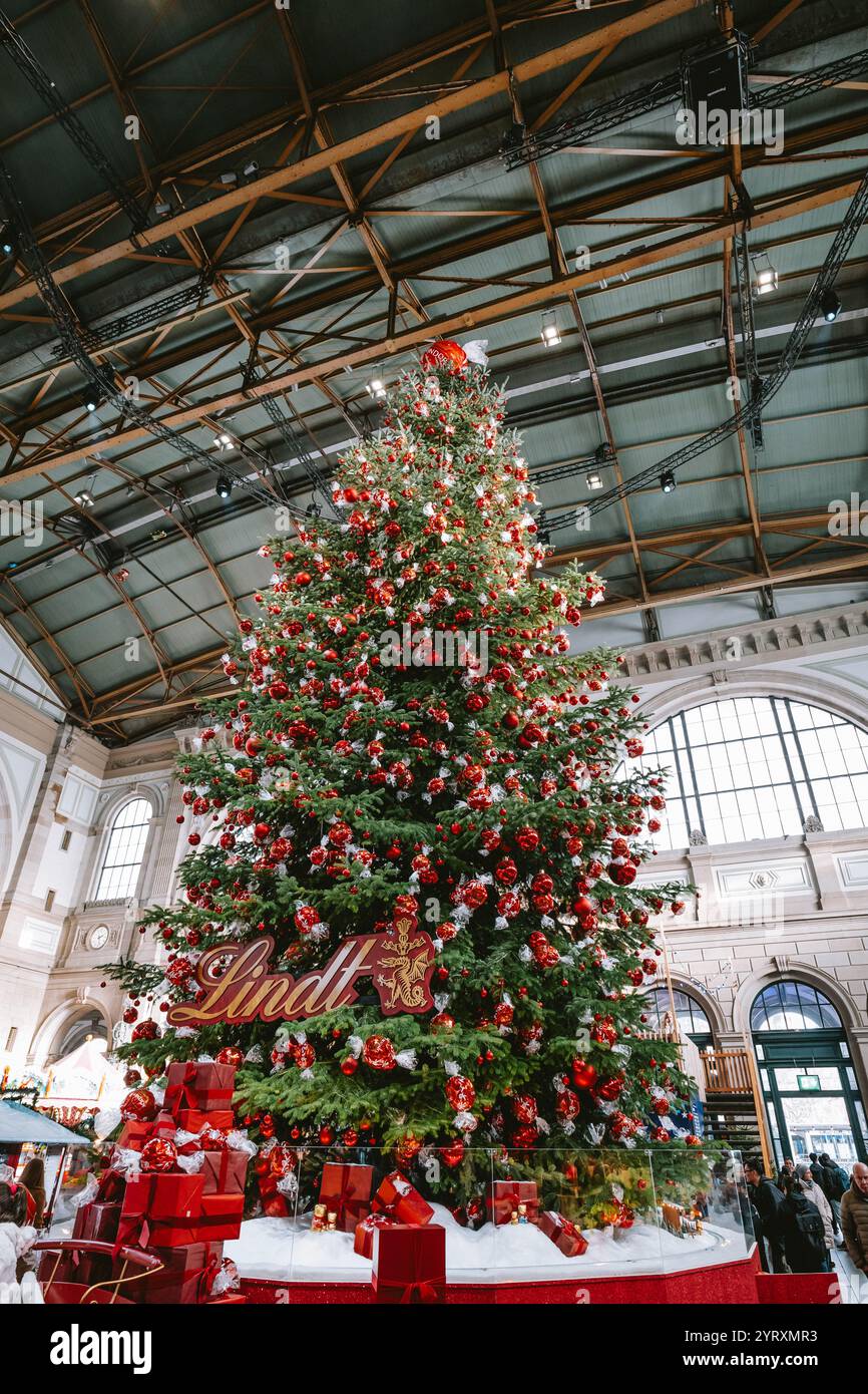 3-12-2024 Zurigo, Svizzera. Grande albero di Natale all'interno della stazione principale di Zurigo decorato con palline di cioccolato Lindt rosse. Grandangolo, mirino verso l'alto, Foto Stock