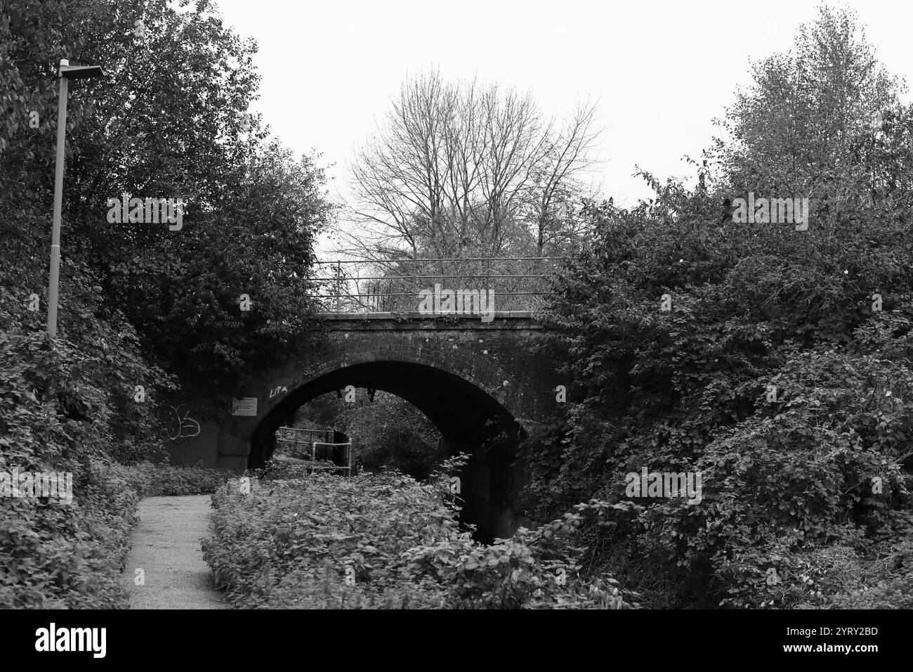 Romsey, Southampton, Inghilterra. 4 novembre 2024. Vista in scala di grigi di un ponte che passa sopra un fiume e un sentiero pedonale. Foto Stock