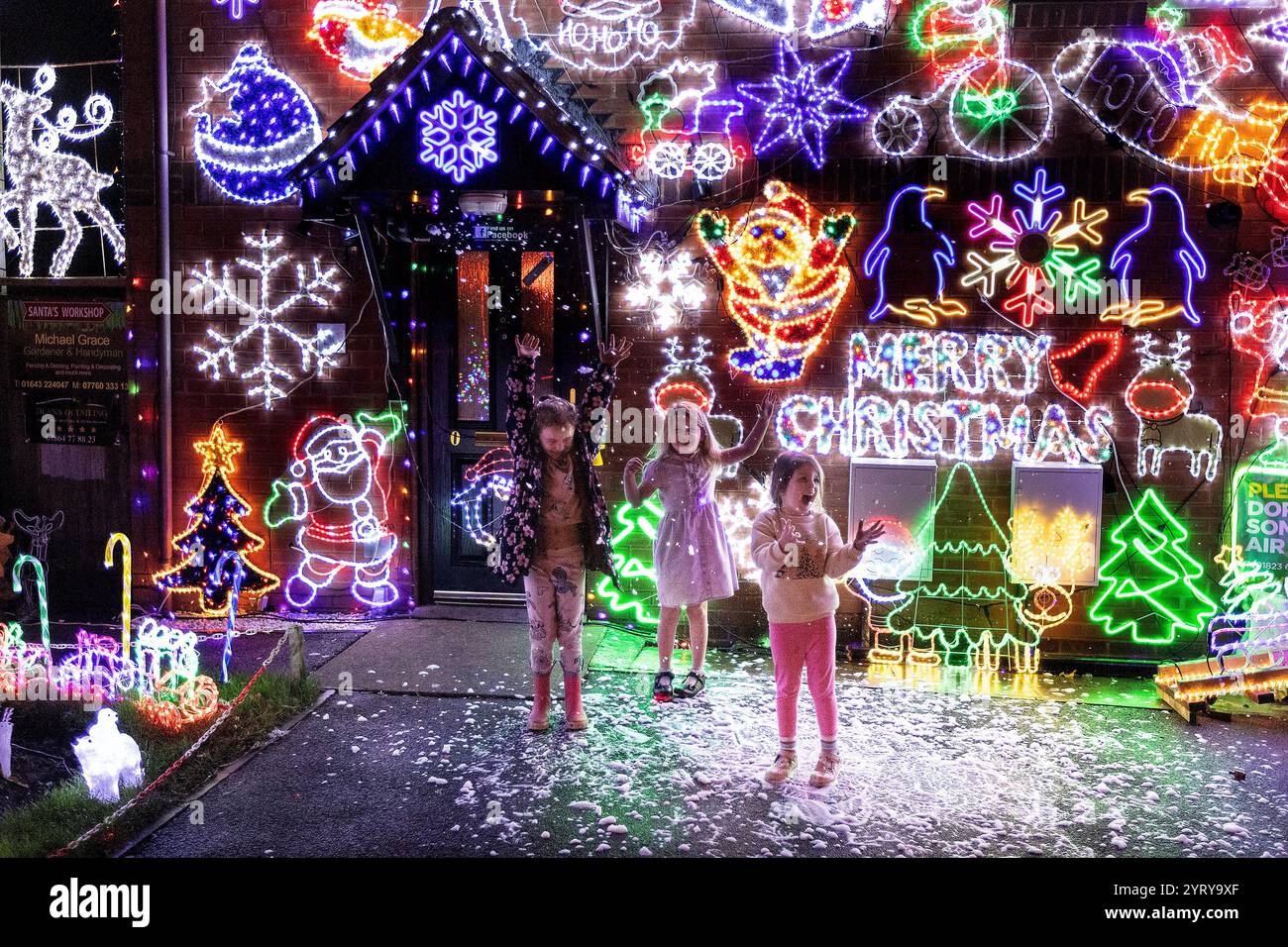 Minehead, Regno Unito. 4 dicembre 2024. Questa è la casa più festosa della Gran Bretagna? Bambini che giocano con la neve, da una macchina da neve, che è una delle caratteristiche della casa. Michael Grace, ha passato gli ultimi dieci anni aumentando dolcemente la quantità di luci natalizie nella sua proprietà a Plover Close a Minehead, Somerset, per far brillare il suo display! Le luci si stanno rivelando un grande richiamo per i visitatori, da quando sono stati accesi il 23 novembre, e stanno raccogliendo fondi vitali per l'ambulanza Dorset e Somerset Air. Credito: Mark Passmore/Alamy Live News Foto Stock