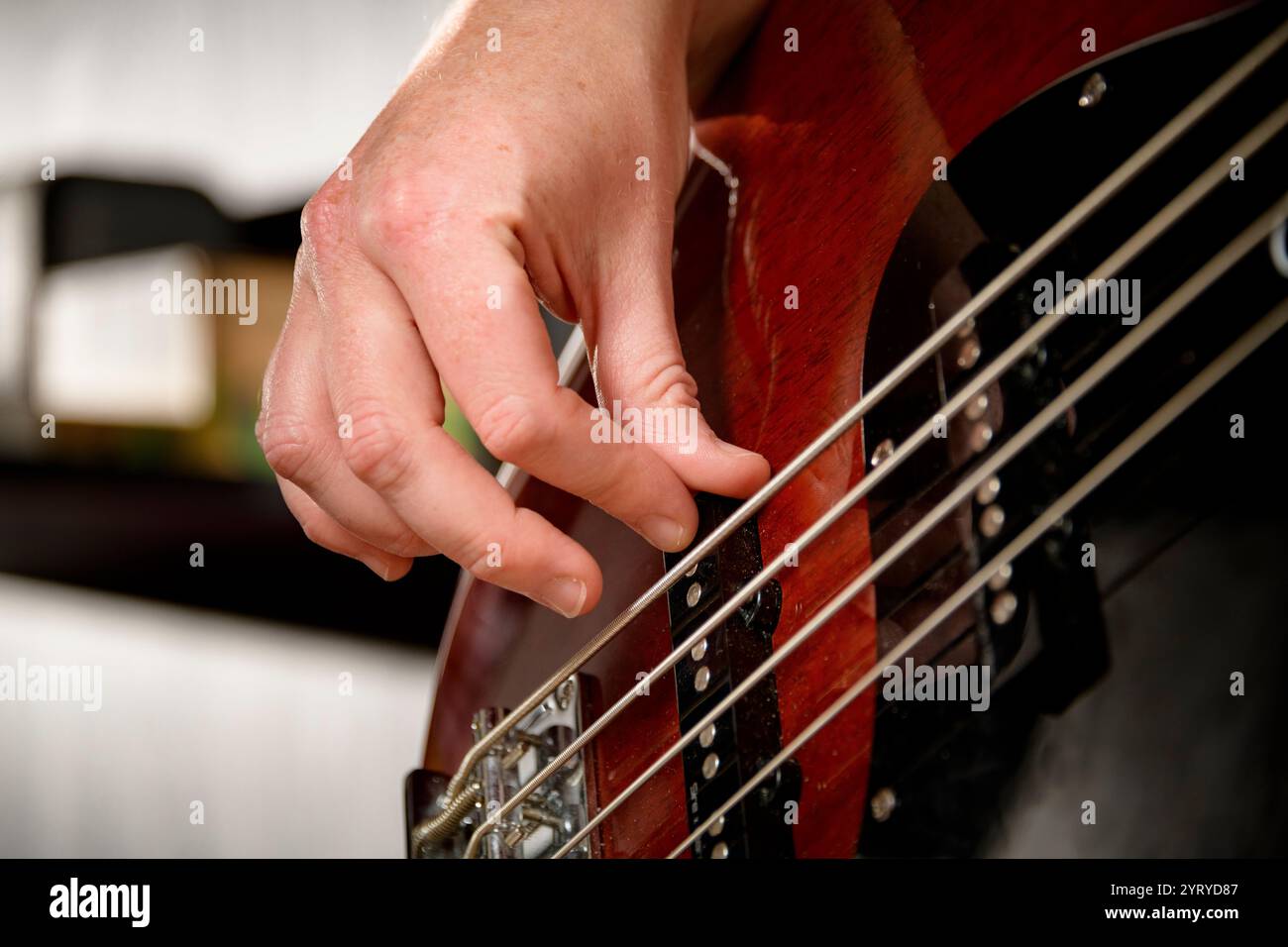 Primo piano della mano di un musicista che toglie le corde di una chitarra basso, enfatizzando le prestazioni musicali, la tecnica e la maestria artigianale. Foto Stock
