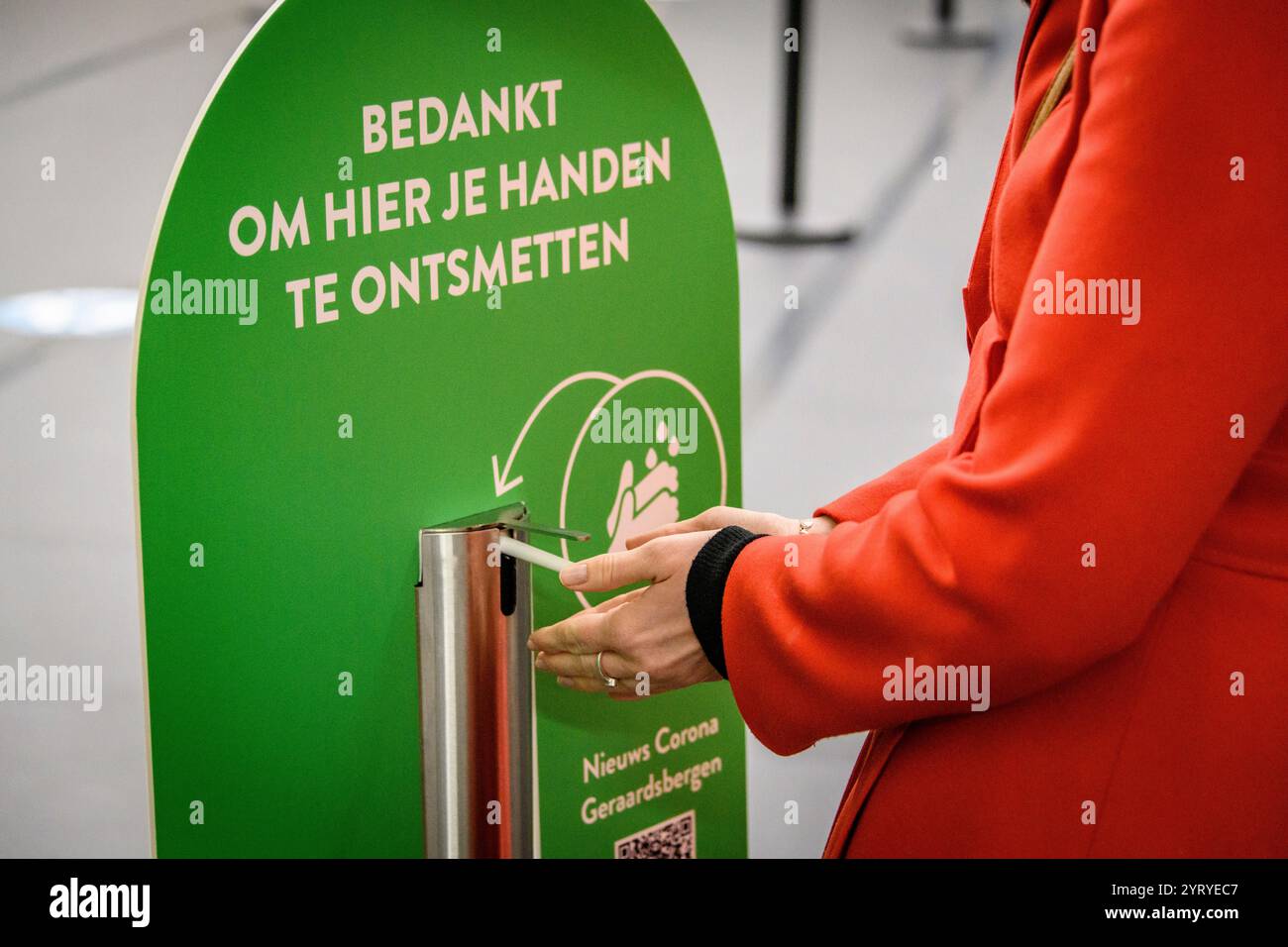 Persona che utilizza una stazione igienizzante per le mani con un cartello olandese che promuove misure di igiene e sicurezza durante la pandemia di COVID-19. Foto Stock