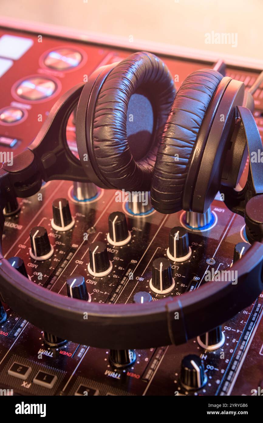 Cuffie che poggiano su una console di mixaggio DJ con una calda illuminazione del palcoscenico, simboleggiano la produzione musicale, la performance dei DJ e la cultura della vita notturna. Foto Stock