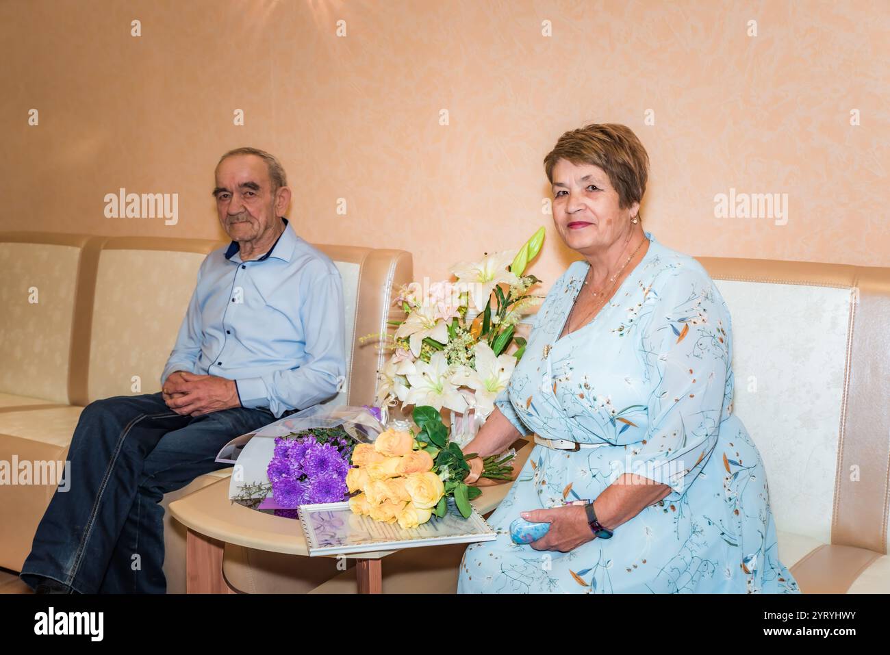Una coppia russa anziana, 71 e 75 anni, si è appena sposata all'ufficio del registro. Si siedono accanto a bouquet floreali, entrambi in abbigliamento blu, a simboleggiare il Foto Stock