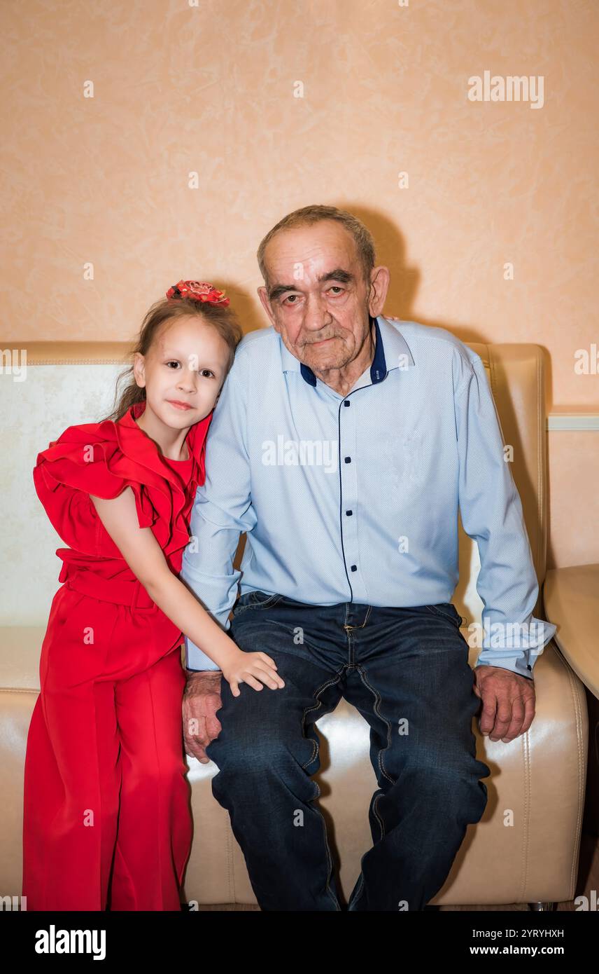 Un nonno russo e sua nipote di 8 anni festeggiano il suo compleanno. Il nonno, 76 anni, e la ragazza sono vestiti festosamente, shar Foto Stock