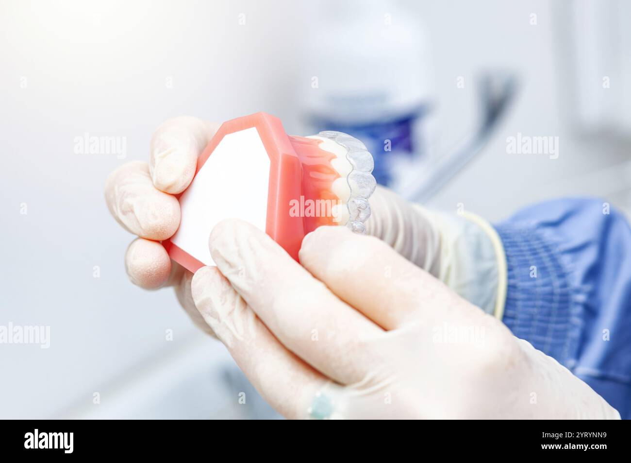 Il dentista che indossa i guanti regge un modello di denti con apparecchi invisibili che ne dimostrano il funzionamento Foto Stock