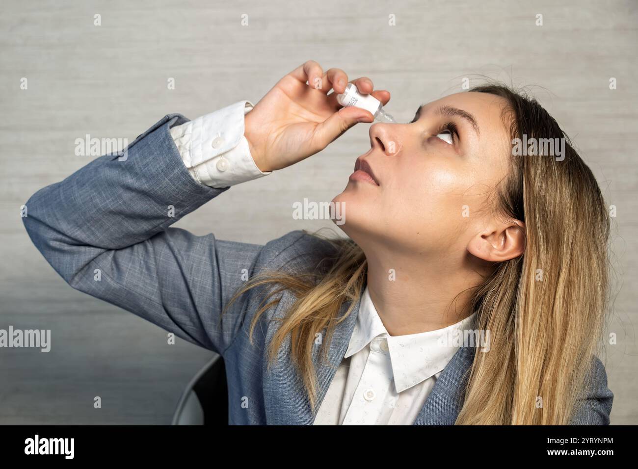 Imprenditrice freelancer che lavora su laptop e tiene gocce medicinali per alleviare lo stress e la secchezza degli occhi, a causa del lavoro eccessivo sul laptop. Digitale Foto Stock