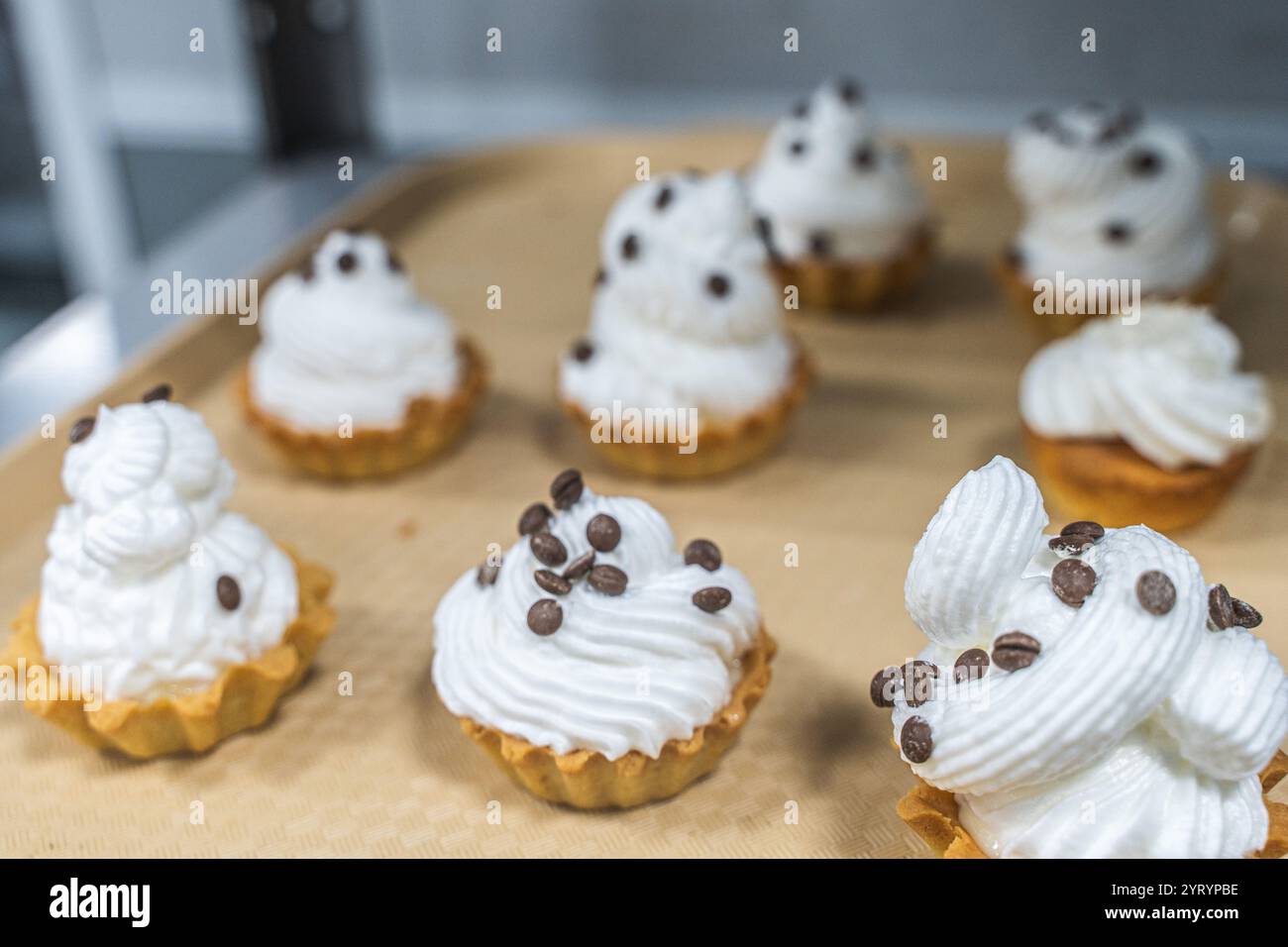 Tortine di pasta frolla con soffice panna bianca o crema, decorate con cioccolato su un vassoio sul tavolo di produzione, in una pasticceria o in un laboratorio. Foto Stock