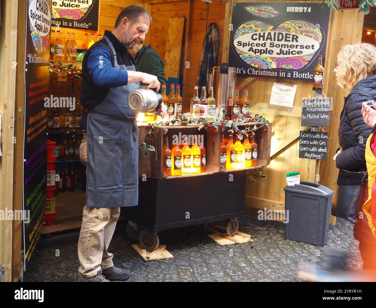 Chaider stalla al mercatino di Natale di Bath che vende succo di mela di Somerset speziato analcolico con il piccolo portabagagli e versa un assaggio per il cliente Foto Stock