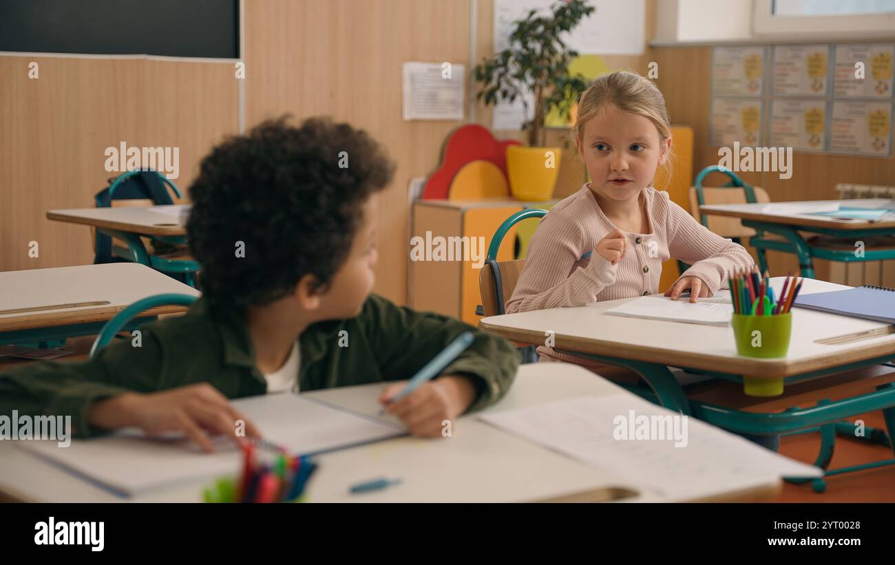 Multirazziale diversi piccoli compagni di classe studenti multietnici alunni due bambini ragazzi ragazza caucasica aiutare ragazzo afroamericano suggerire una risposta corretta a. Foto Stock