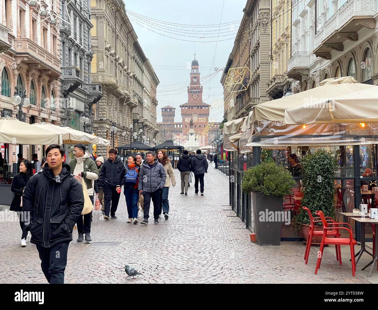 Milano, Italia - 25 novembre 2024. La gente cammina lungo la strada con le luci natalizie nel centro della città vicino al Duomo con il Castello Sforzesco sullo sfondo Foto Stock