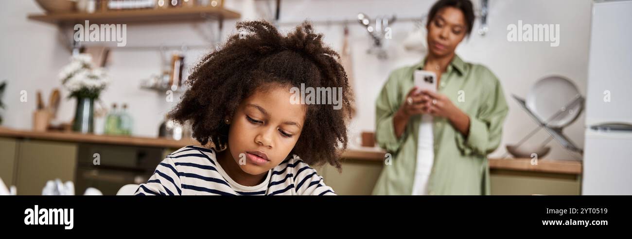 In una cucina calda, una madre guarda con amore sua figlia si concentra sul suo disegno. Foto Stock