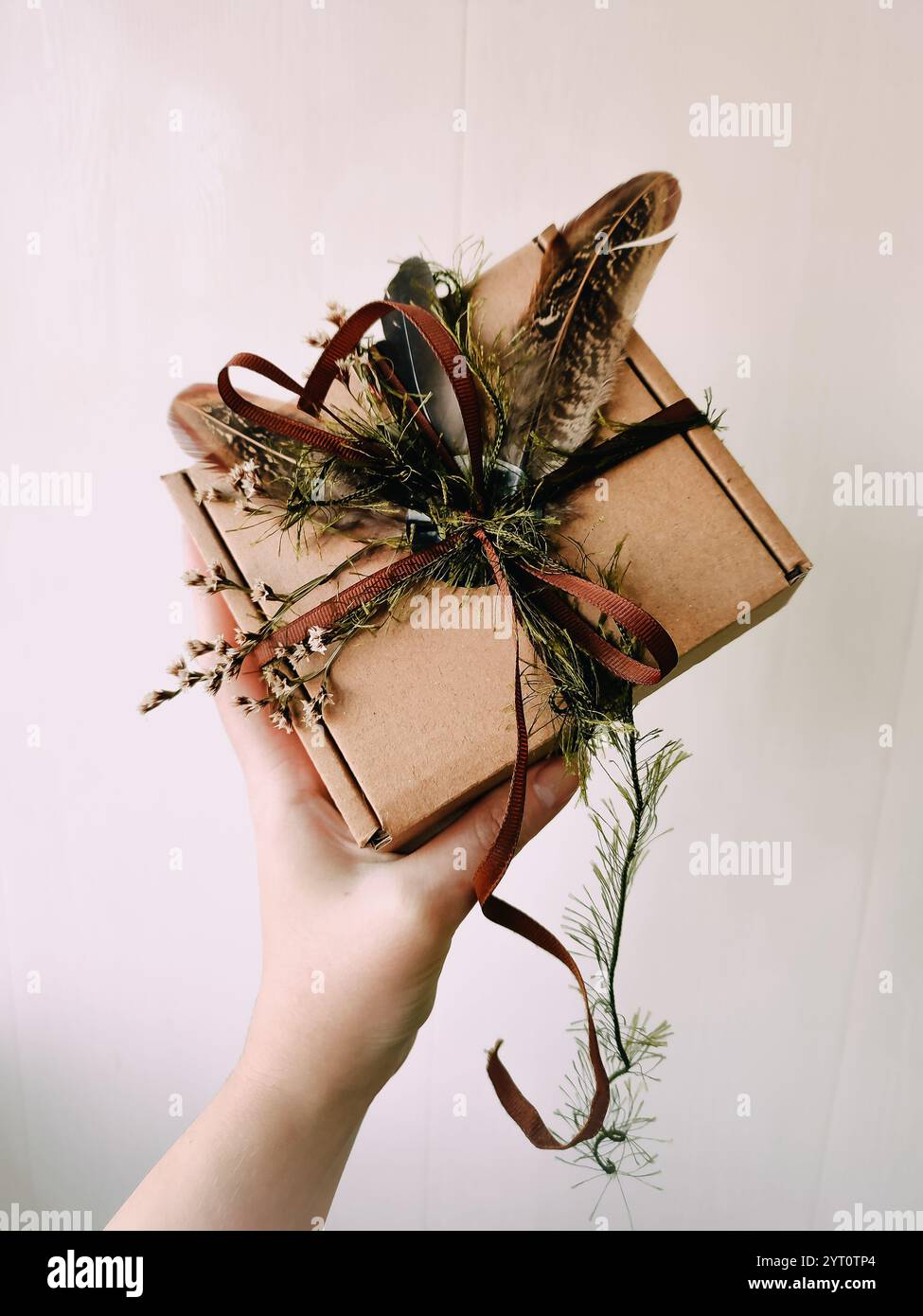 Imballaggio artigianale, imballaggio, scatola, pacco. Scatola di carta marrone decorata con erbe essiccate, piume, nastro, nastri a portata di mano. Prodotto artigianale, vacanze Foto Stock