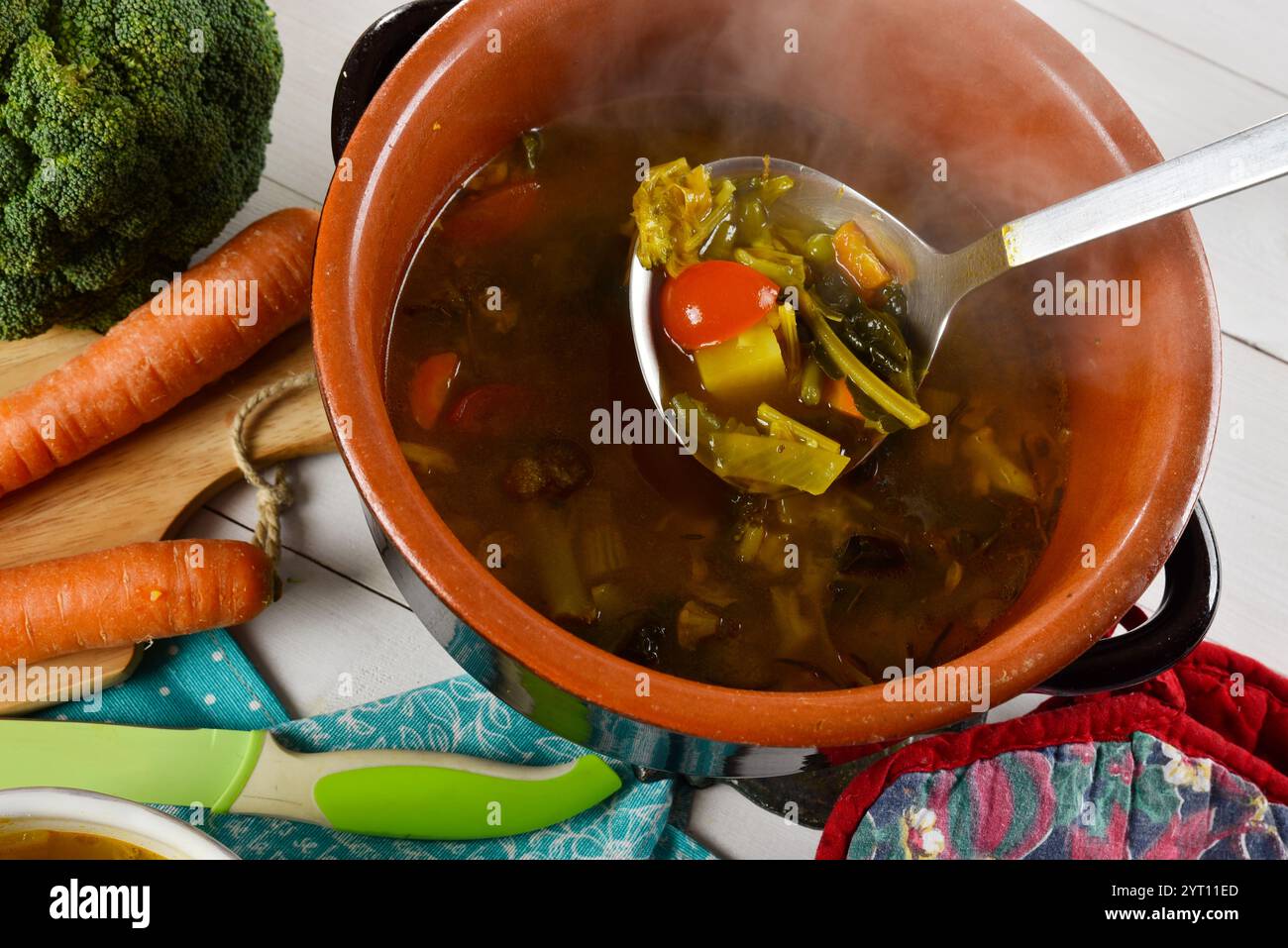 Zuppa di verdure calda in una padella di terracotta con un mestolo di zuppa fumante Foto Stock