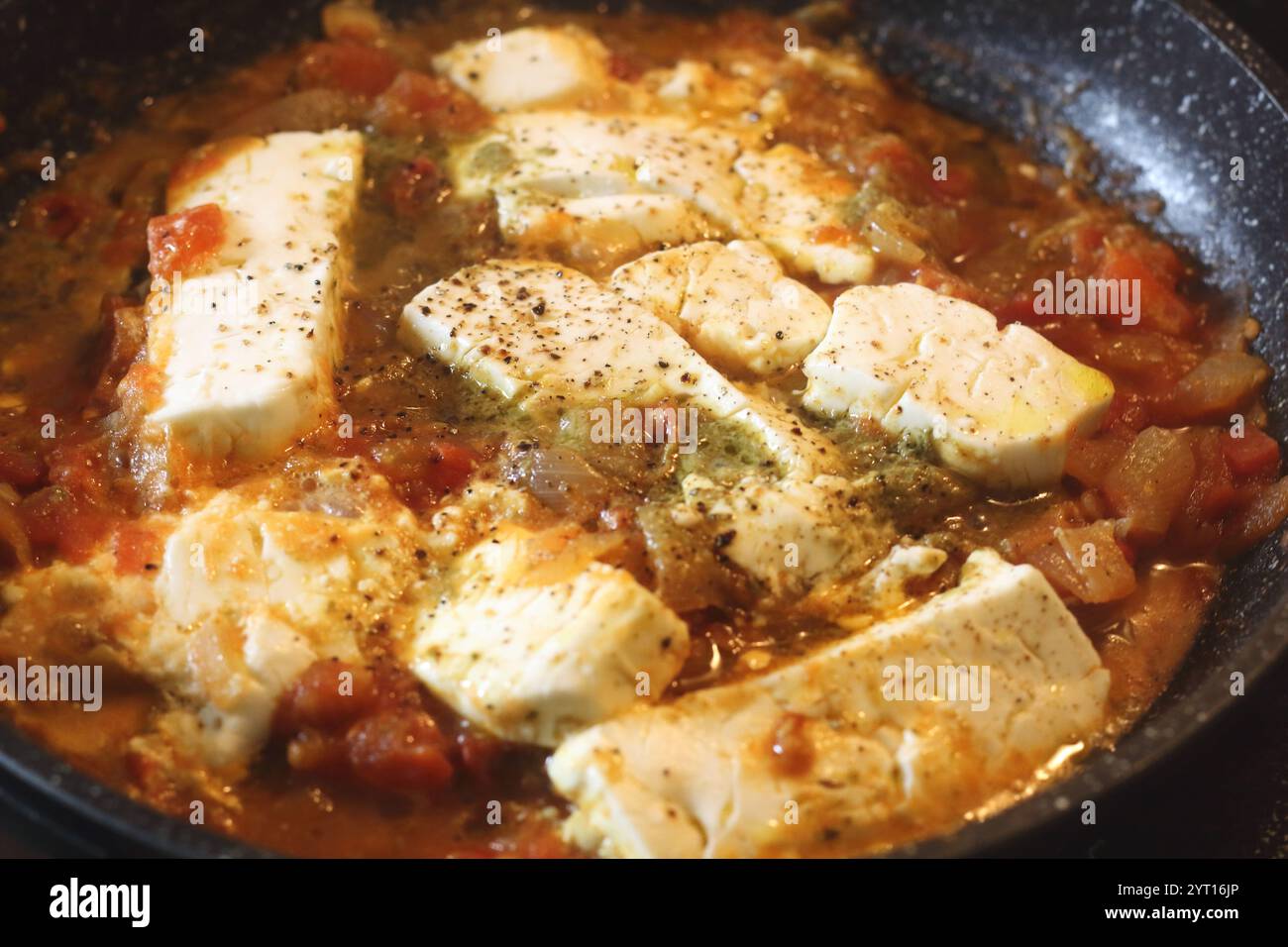 Un vibrante shot di Bougiourdi, un piatto tradizionale greco cotto al forno, con cremoso formaggio feta, succosi pomodori, cipolle dolci e piccante colorato Foto Stock