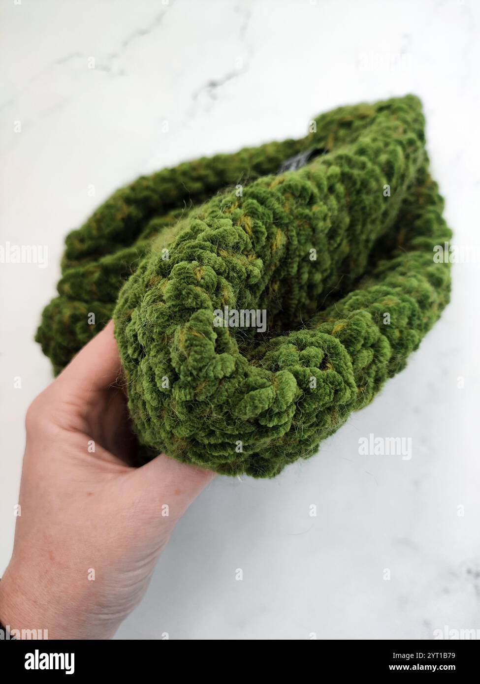 Berretto a maglia in velluto verde a mano su sfondo in marmo bianco, cappello in muschio grosso, copricapo caldo e accogliente, accessorio, abbigliamento, motivo a maglia Foto Stock