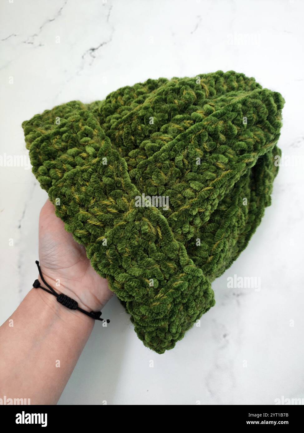 Berretto a maglia in velluto verde a mano su sfondo in marmo bianco, cappello in muschio grosso, copricapo caldo e accogliente, accessorio, abbigliamento, motivo a maglia Foto Stock