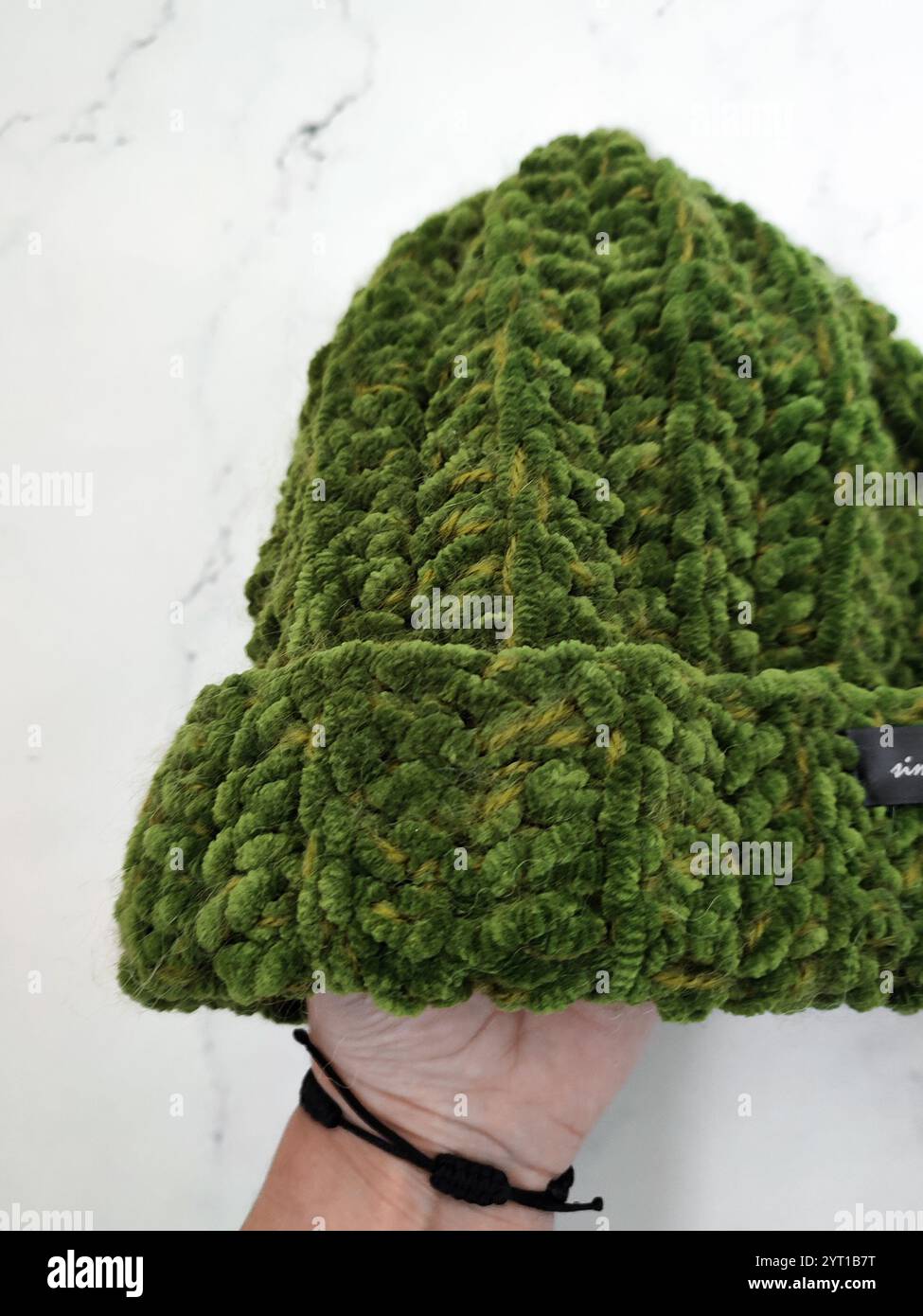 Berretto a maglia in velluto verde a mano su sfondo in marmo bianco, cappello in muschio grosso, copricapo caldo e accogliente, accessorio, abbigliamento, motivo a maglia Foto Stock