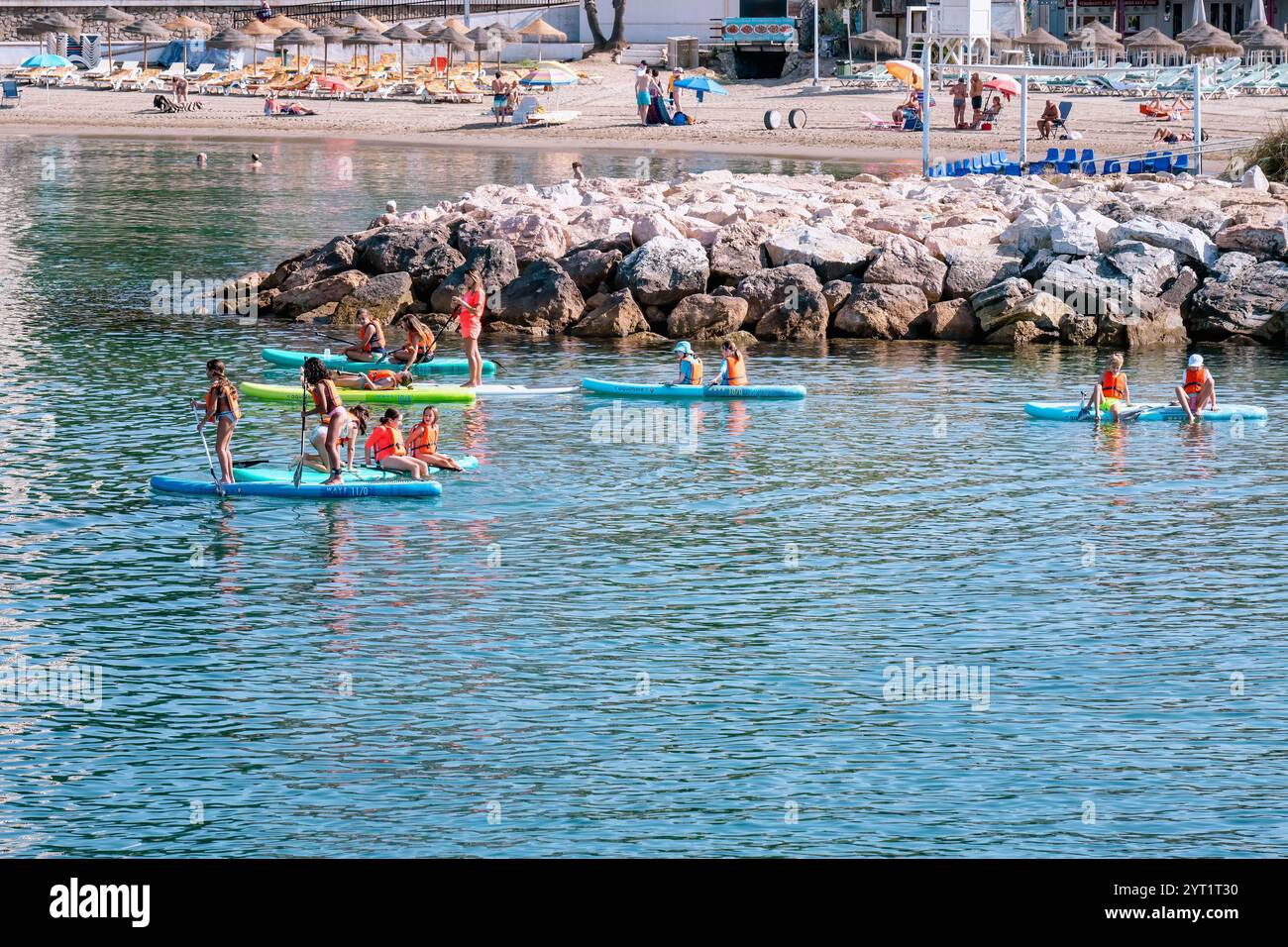 Adolescenti che si divertono con sport acquatici, kayak e paddle boarding, nelle calme acque del Mediterraneo vicino a una spiaggia Foto Stock
