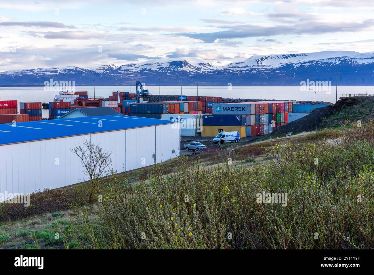 Husavik, Islanda, 21.05.22. Contenitori di spedizione immagazzinati nel porto di Husavik con montagne innevate sullo sfondo. Foto Stock