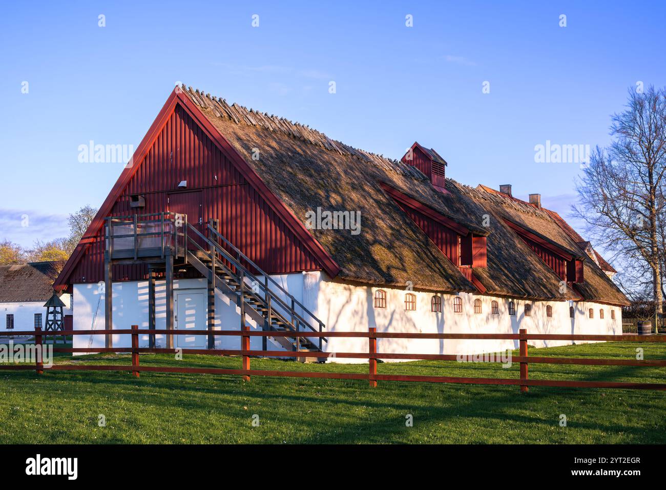 Malmö, Svezia - 24 aprile 2024: Un fienile rustico, recentemente ristrutturato per negozi con facciata rossa e un tetto ripido, situato in una zona erbosa sotto un cielo blu, Place Foto Stock