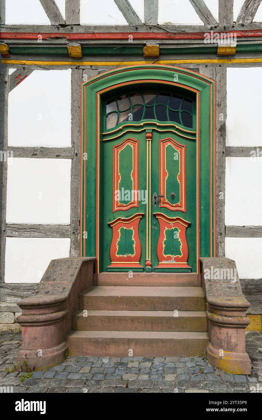 Una vibrante porta tradizionale in legno verde e rosso con motivi intricati e intagli decorativi, incorniciata da una facciata bianca e in legno. Foto Stock