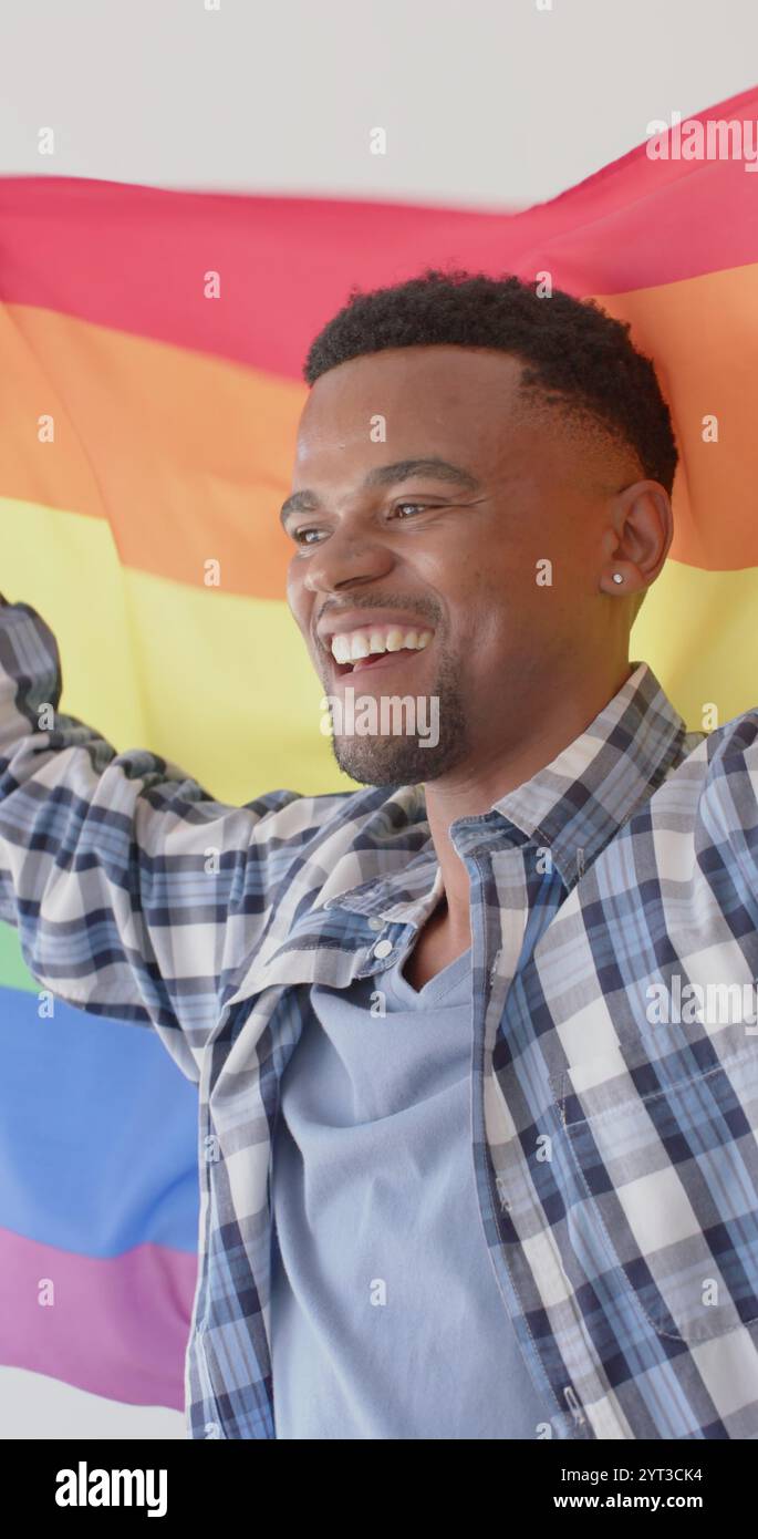 Immagine verticale di un uomo afroamericano felice con bandiera arcobaleno lgbt Foto Stock