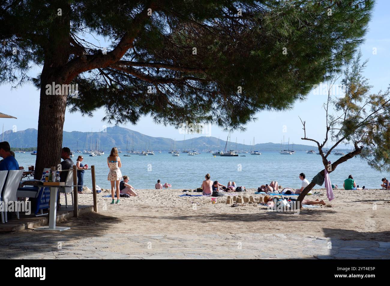 La spiaggia di Port de Pollenca, vista dal Pine Walk, con la gente sedeva ai tavoli del ristorante in primo piano nelle Isole Baleari di Maiorca Foto Stock