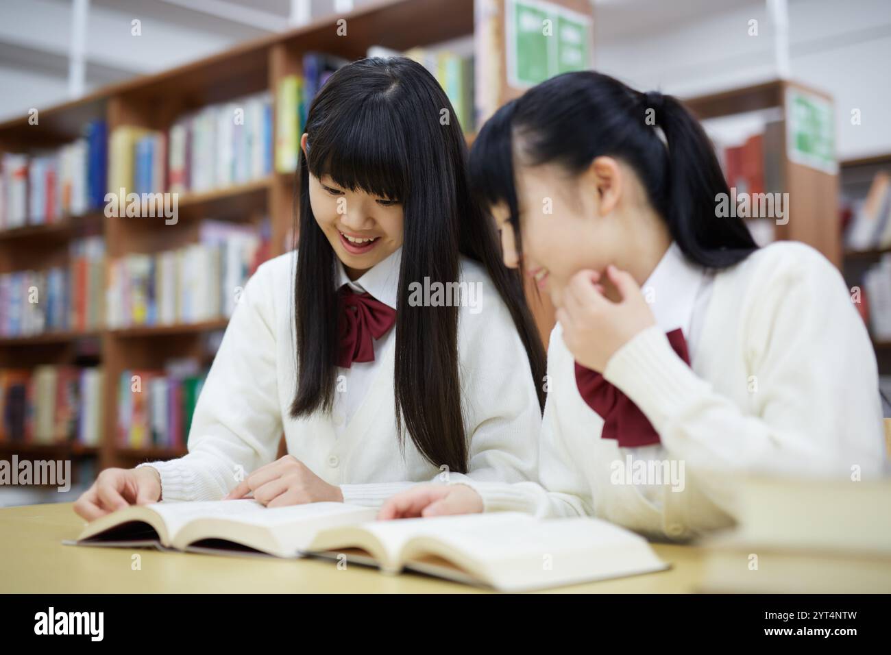 Studentessa delle superiori che legge un libro in biblioteca Foto Stock