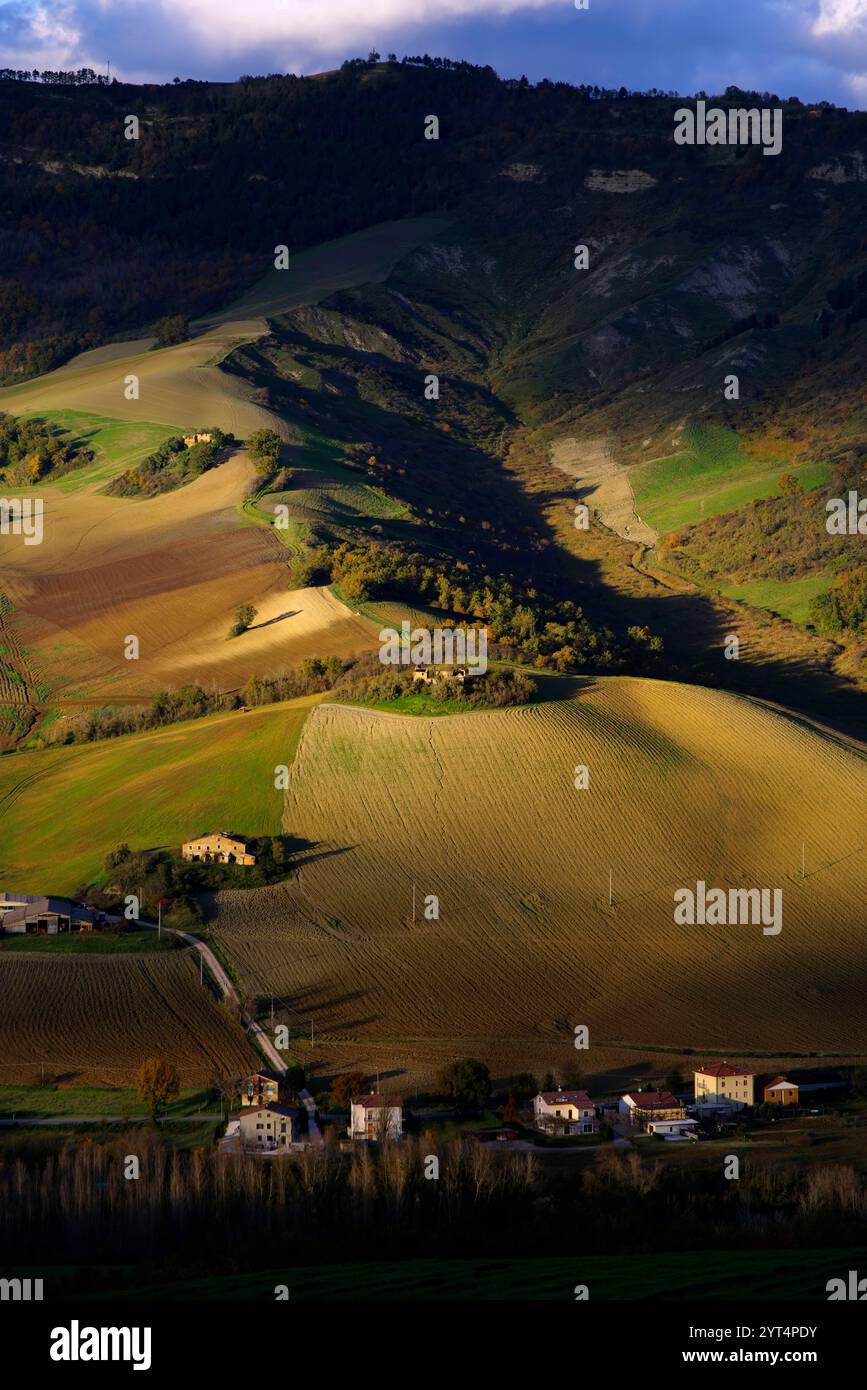 Panorama di campi e colline del Montefeltro in autunno nell'ora d'oro contro il cielo nuvoloso Foto Stock