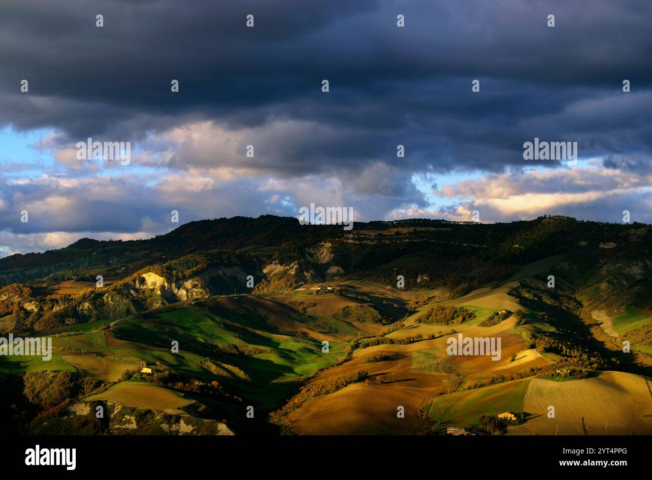Panorama di campi e colline del Montefeltro in autunno nell'ora d'oro contro il cielo nuvoloso Foto Stock