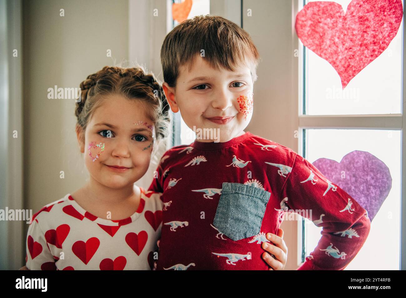I fratelli con il trucco con il cuore glitter posano alla finestra con decorazioni Foto Stock