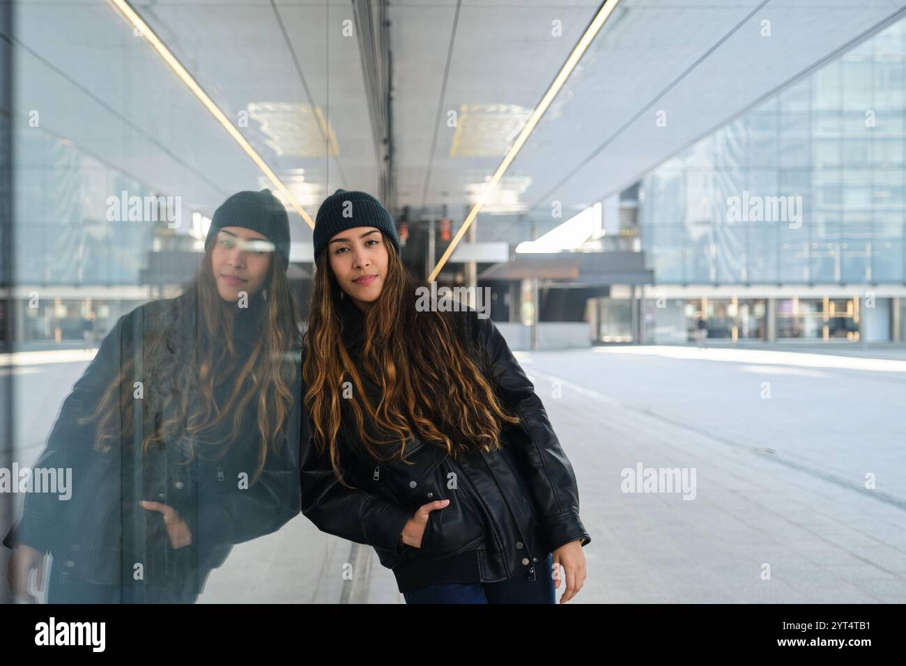 Giovane donna urbana appoggiata su un muro di vetro nella città moderna Foto Stock