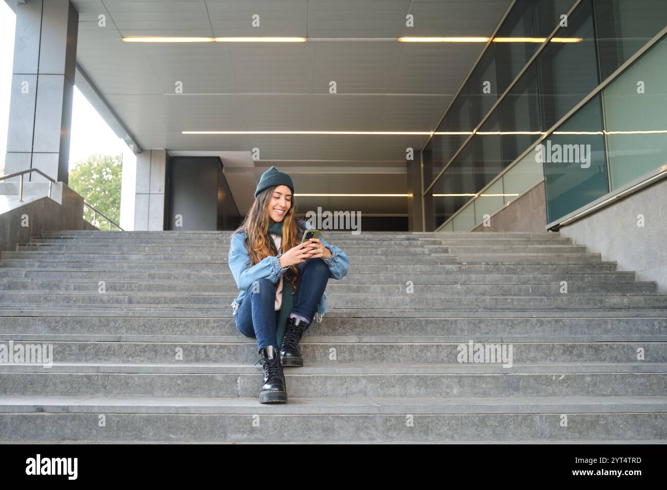 Studente sorridente che usa lo smartphone seduto sui gradini dell'università Foto Stock