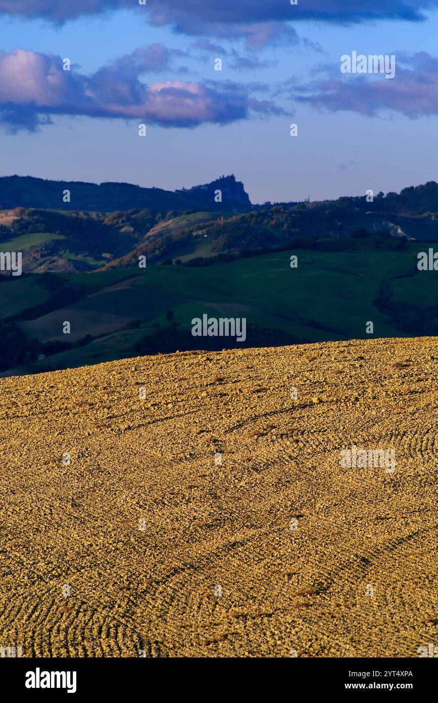 Panorama di campi e colline del Montefeltro in autunno nell'ora d'oro contro il cielo nuvoloso Foto Stock