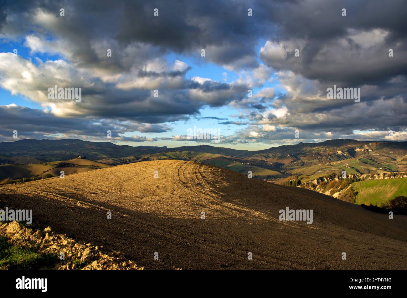 Panorama di campi e colline del Montefeltro in autunno nell'ora d'oro contro il cielo nuvoloso Foto Stock