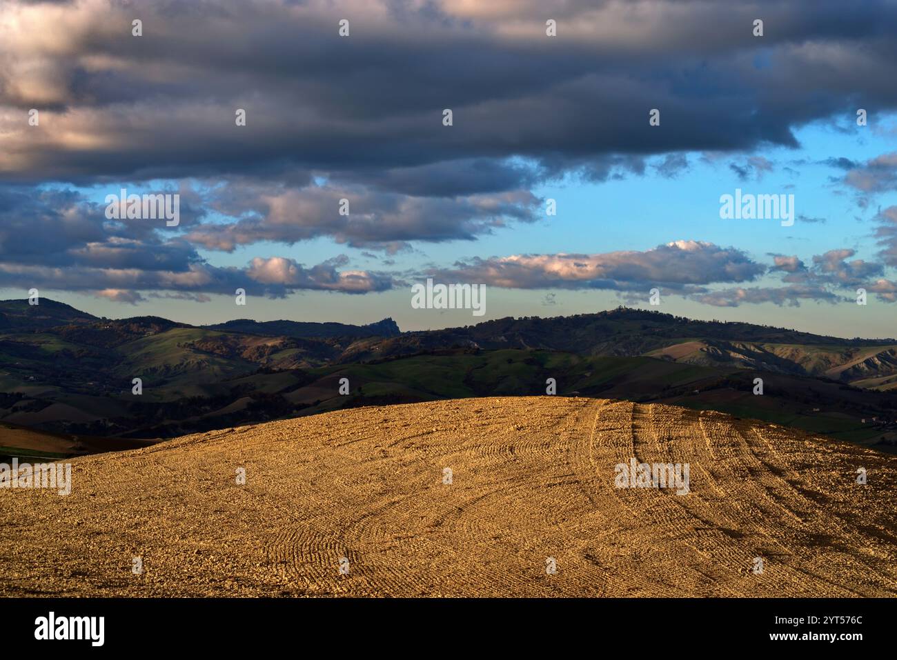 Panorama di campi e colline del Montefeltro in autunno nell'ora d'oro contro il cielo nuvoloso Foto Stock