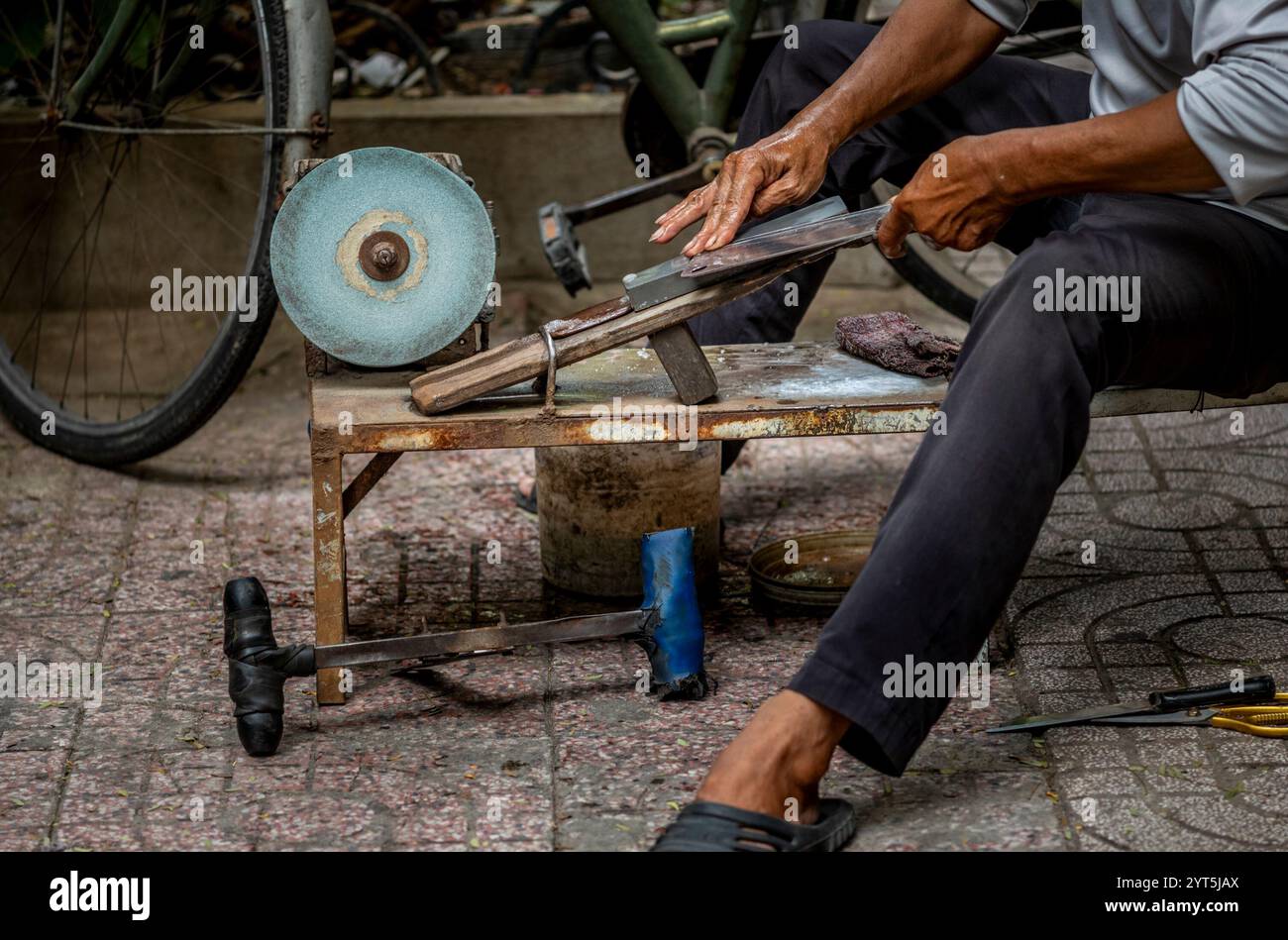 Un uomo che affila i coltelli a mano per le strade di Saigon in Vietnam Foto Stock