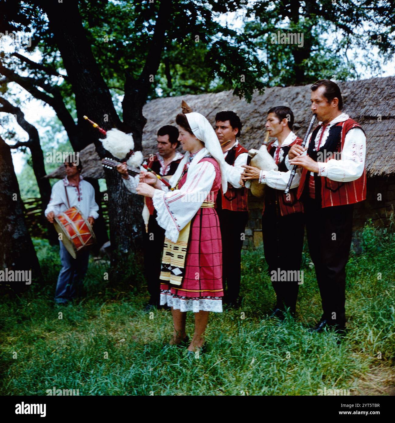 Eine Frau in traditionellem Spreewälder Gewand , Spreewald Tracht, demonstriert die Handwerkskunst der Spinnerei, dazu spielt ein kleines Orchester, vermutlich im Rahmen des Lübbenauer Spreewaldfestes (?), DDR um 1975. Foto Stock