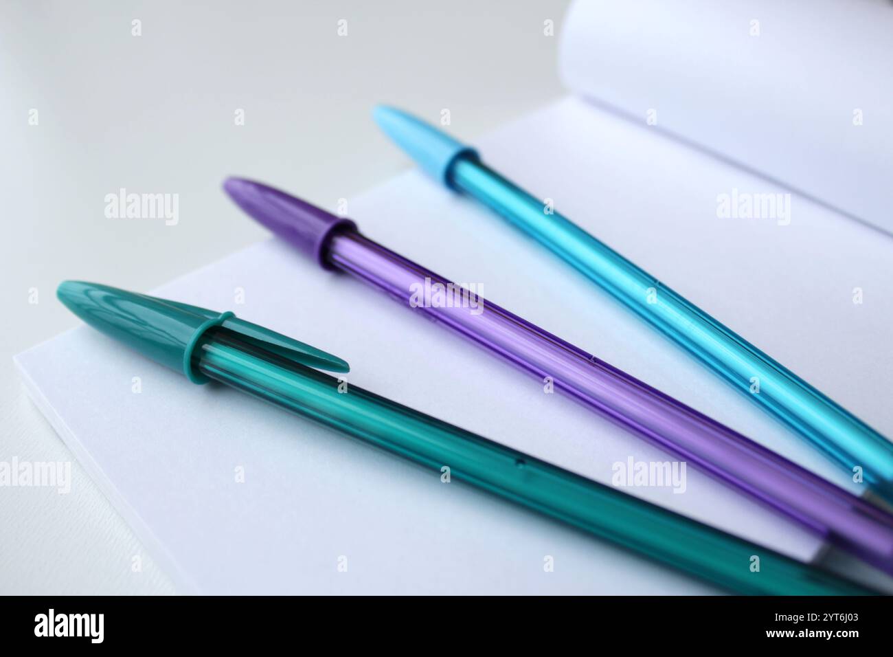 Tre penne colorate fredde sulla parte superiore di una pagina di blocco note in carta bianca. Penna a sfera verde, viola e blu. Cartoleria creativa per attività di ritorno a scuola. Foto Stock