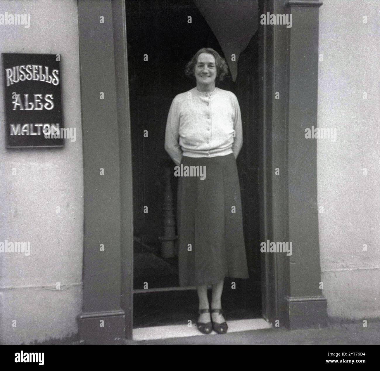 Anni '1950, storica, una signora che si ferma per una foto all'ingresso di un pub, Star Inn, rivenditore autorizzato di birre, vini, liquori e tabacco, una Samuel Cherry. Il cartello sul muro dice Russells Ales Malton, North Yorkshire, Inghilterra, Regno Unito, che risale al 1771. Russells & Wrangham Ltd, Derwent Brewery, Castlegate, Malton, North Yorkshire nacque nel 1897 con la fusione di James Russell & Son e William Wrangham Ltd Foto Stock