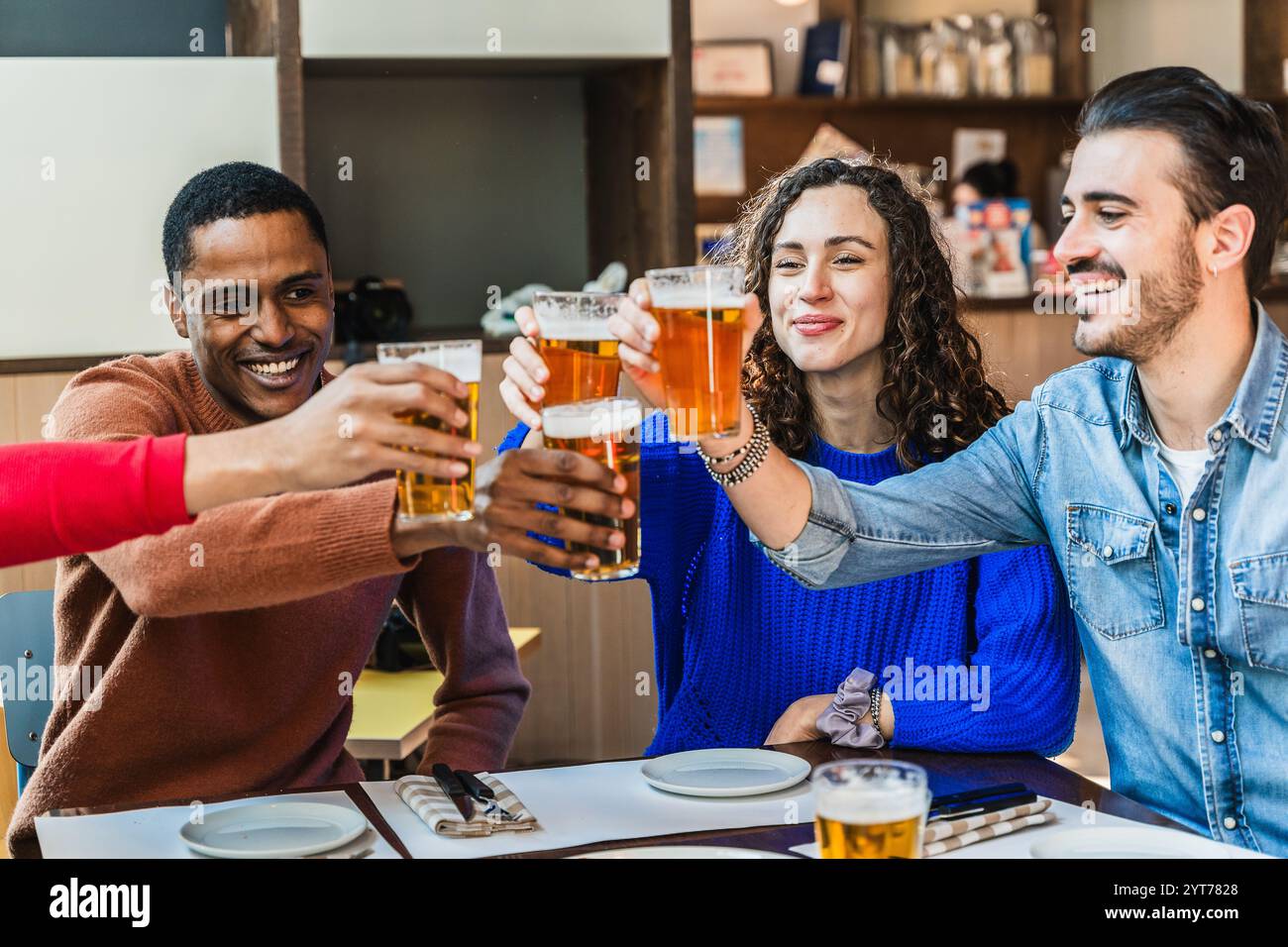 Allegri amici multietnici brindano con bicchieri da birra mentre si divertono insieme al ristorante della birreria Foto Stock