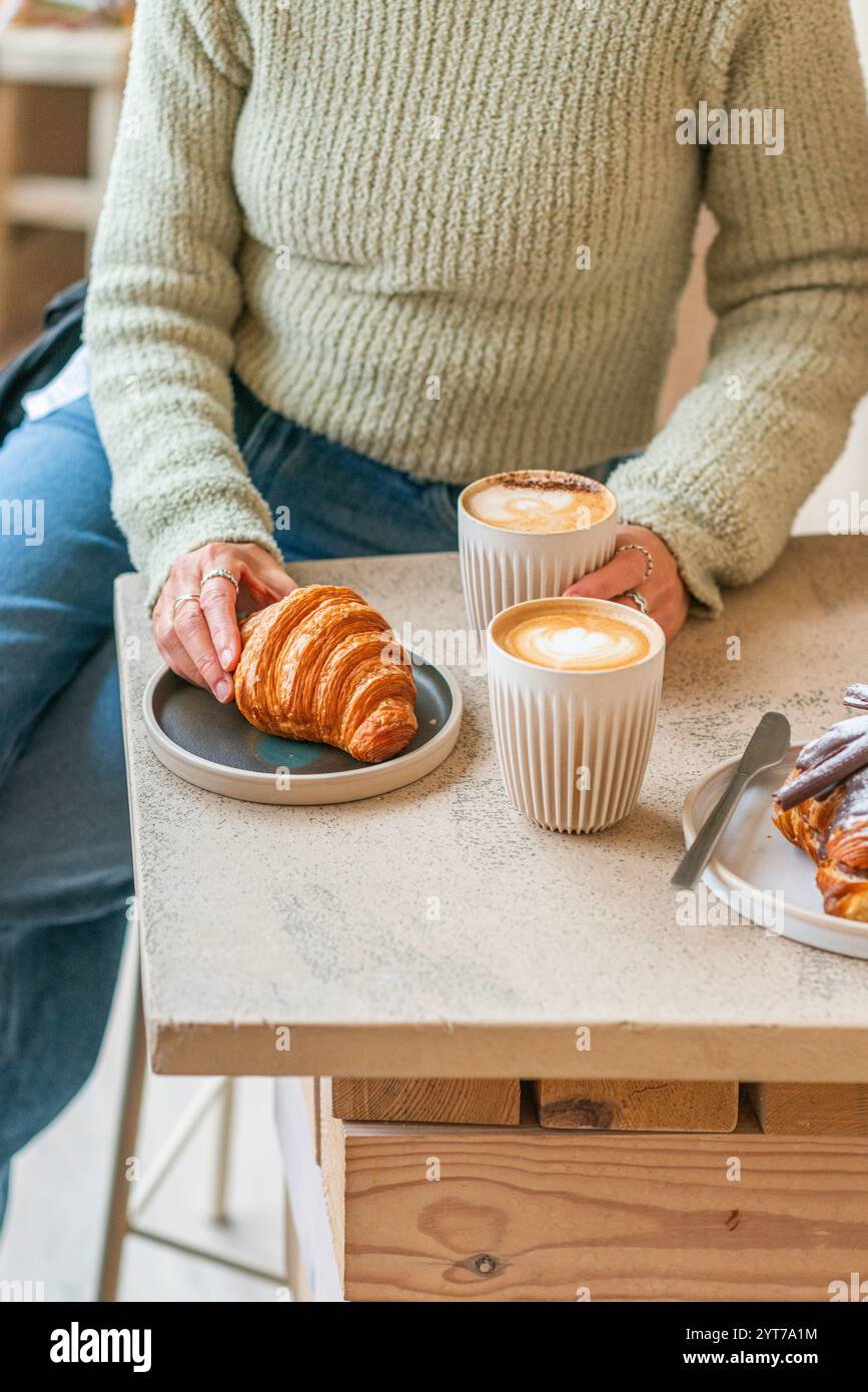 Un caffè minimalista con due cappuccini in tazze in ceramica a coste e due dolci: Un croissant dorato e un croissant al cioccolato. Foto Stock