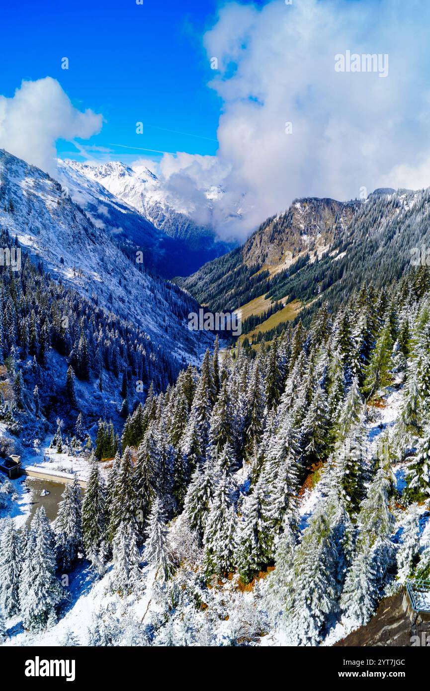 Una vista affascinante della pittoresca valle alpina in una soleggiata giornata invernale. Le nuvole toccano le vette della montagna. Vista verticale Foto Stock